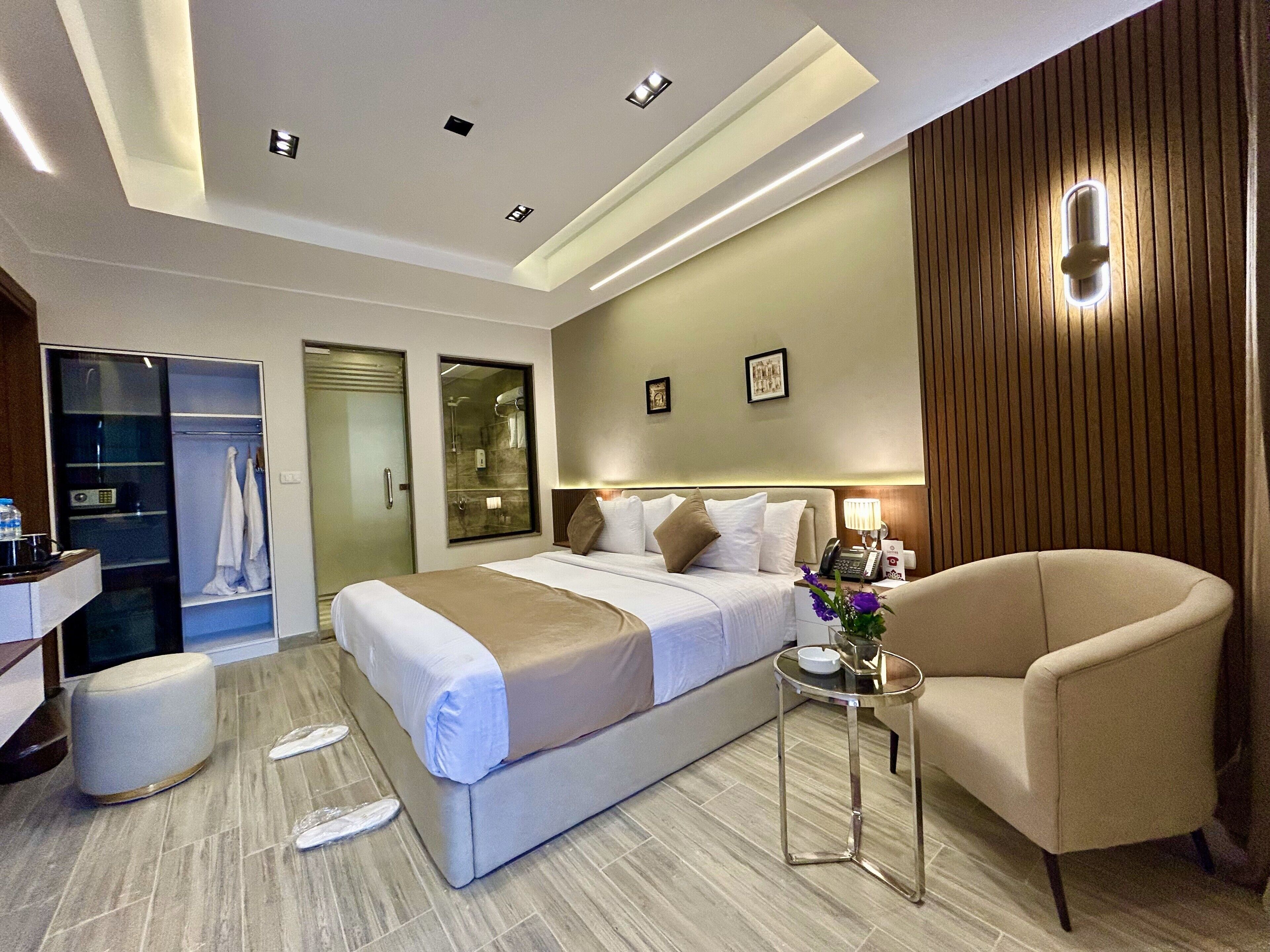 A modern hotel room with a large bed, a sitting area, a vanity, and a shower area.