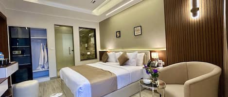 A modern hotel room with a large bed, a sitting area, a vanity, and a shower area.