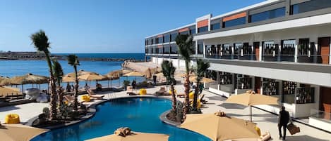 A modern hotel with a pool, lounge chairs, and umbrellas.