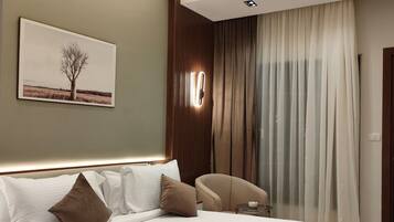 A modern hotel room with a large bed, a chair, a painting of a tree, and a view of the outdoors through a window.