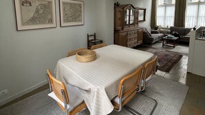 Un coin repas avec une table, des chaises et un lustre. Deux cartes encadrées sont accrochées au mur.
