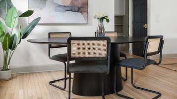 A modern dining area with a round table, black chairs, a large abstract painting, and a unique gold chandelier.