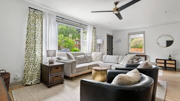 A modern living room with a sectional sofa, a black leather armchair, a round coffee table, and a ceiling fan.