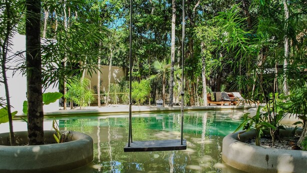 A serene outdoor pool area with a swing, surrounded by lush greenery and a clear blue pool. - Esencia Botanic Piscina Privada  (Tulum)