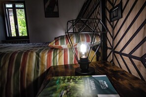 A room with a bed, a table with a lamp, a book, and a window with a view.