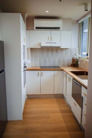 Une cuisine compacte avec des meubles blancs, un plan de travail en bois et un four encastré.