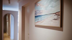 A hallway with a framed painting of a beach scene on the wall.