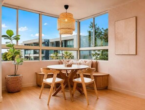 Ein modernes Interieur mit einem runden Holztisch, vier Stühlen, einer gewebten Pendelleuchte und großen Fenstern mit Blick auf Gebäude und Grünflächen.