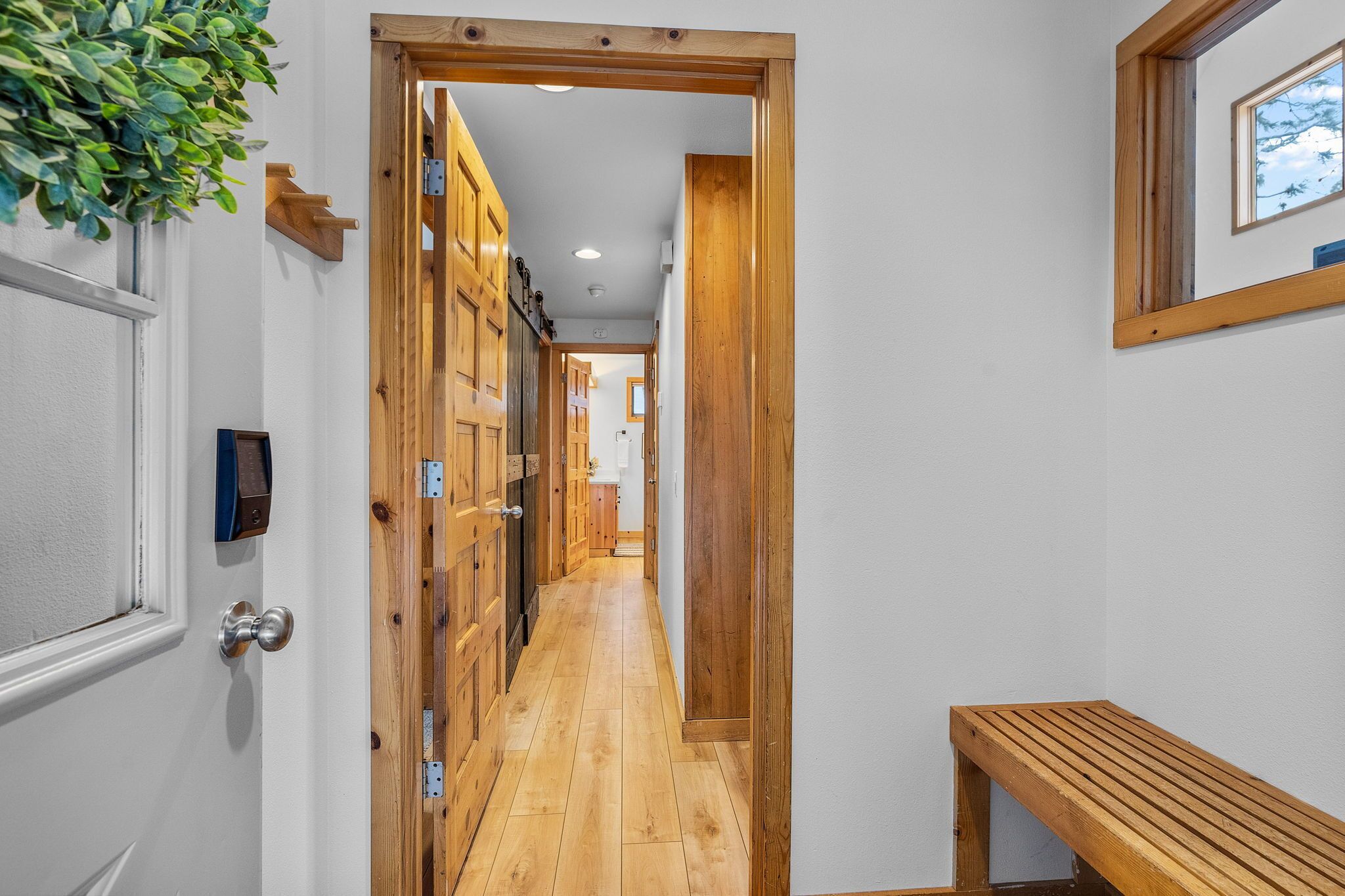A narrow hallway with wooden flooring and doors, a bench, and a plant.