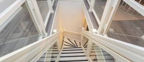 A spiral staircase with glass railings and a white handrail, leading to an upper floor.