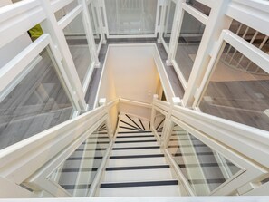 A spiral staircase with glass railings and a white handrail, leading to an upper floor.