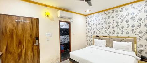 A bedroom with a bed, wooden door, ceiling fan, and patterned wallpaper.