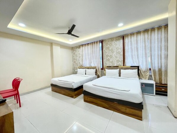 A hotel room with two single beds, a desk with a chair, a ceiling fan, and a window with curtains.