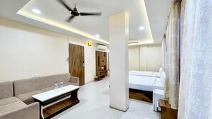 A modern hotel room with a sofa, a bed, a small table, and a ceiling fan. - Hotel Rudra - near Ghats and Temple (Varanasi)
