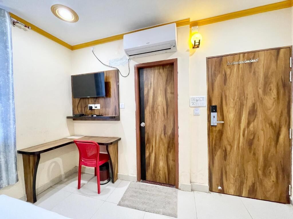 Habitació amb escriptori de fusta, cadira vermella, televisió penjada a la paret i dues portes de fusta.