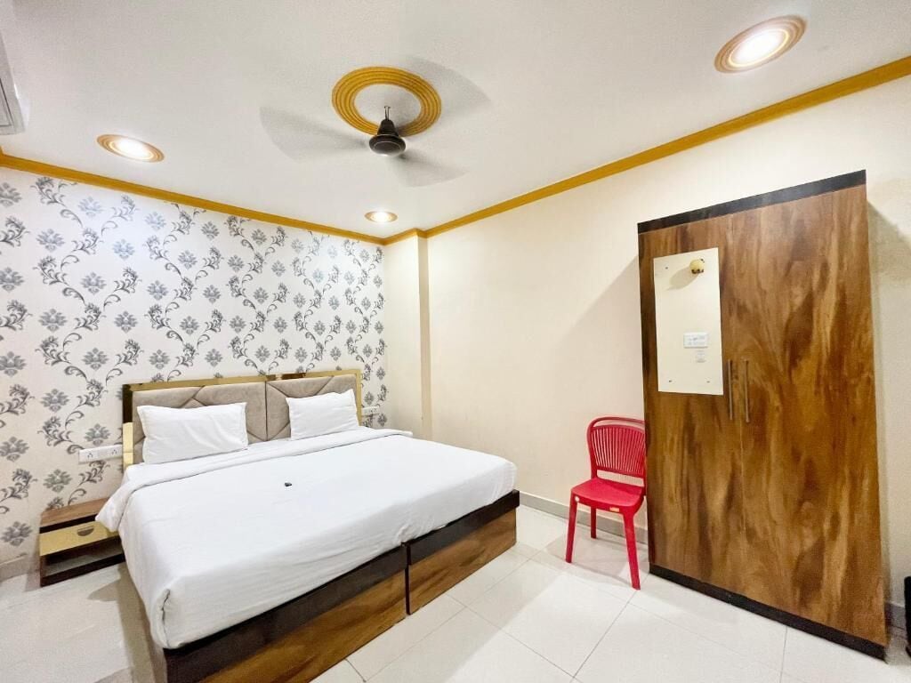 Un dormitorio con una cama, una silla roja, un armario de madera y papel tapiz estampado.