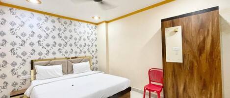 A bedroom with a bed, a red chair, a wooden wardrobe, and patterned wallpaper.
