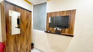 A room with a wooden wardrobe, a mirror, a television mounted on the wall, and a red chair. - Hotel Rudra - near Ghats and Temple (Varanasi)