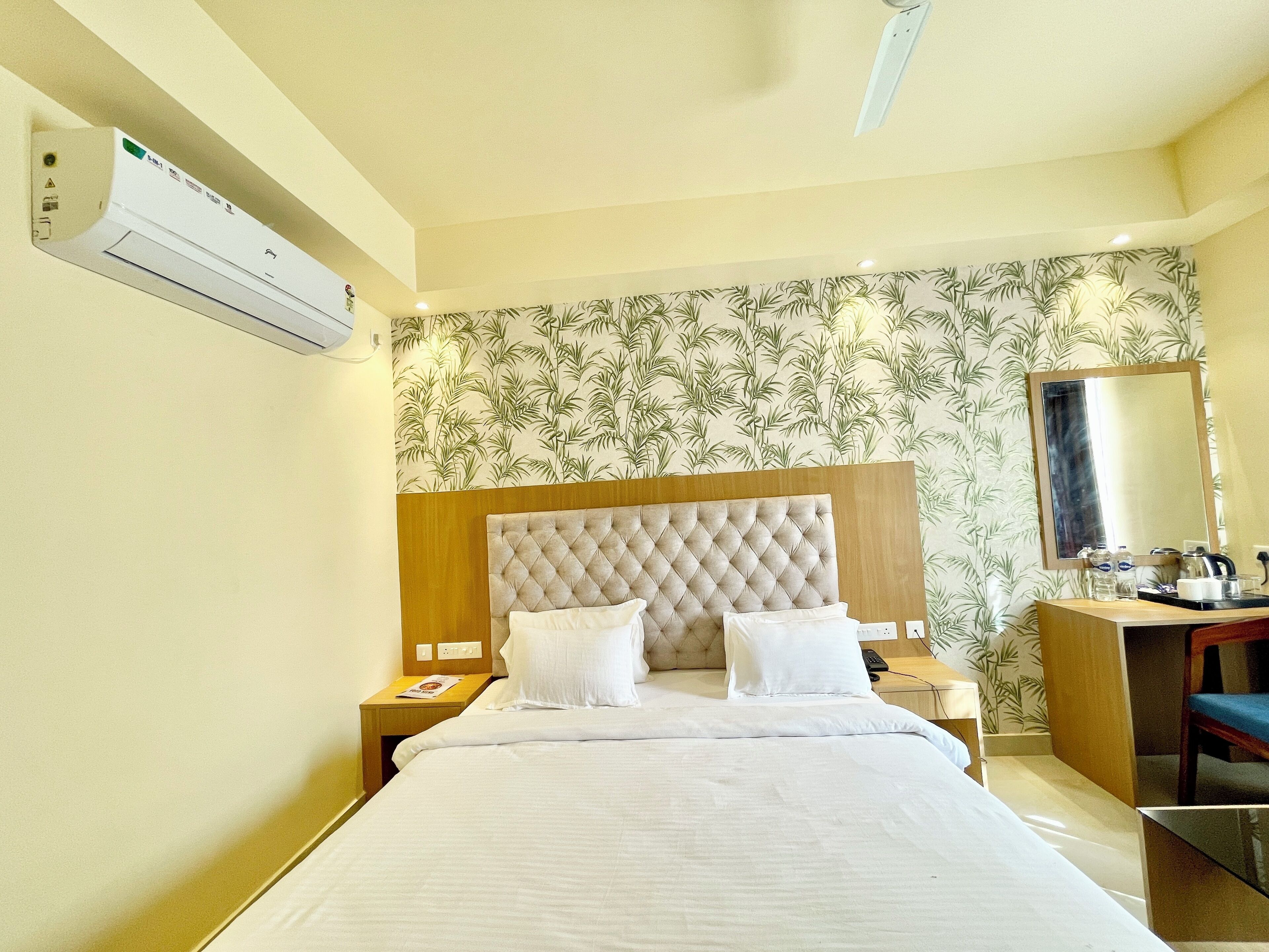 A hotel room with a bed, nightstands, a desk, a chair, a mirror, and an air conditioning unit.