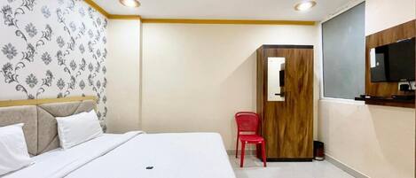 A hotel room with a bed, a red chair, a ceiling fan, and a television mounted on the wall.