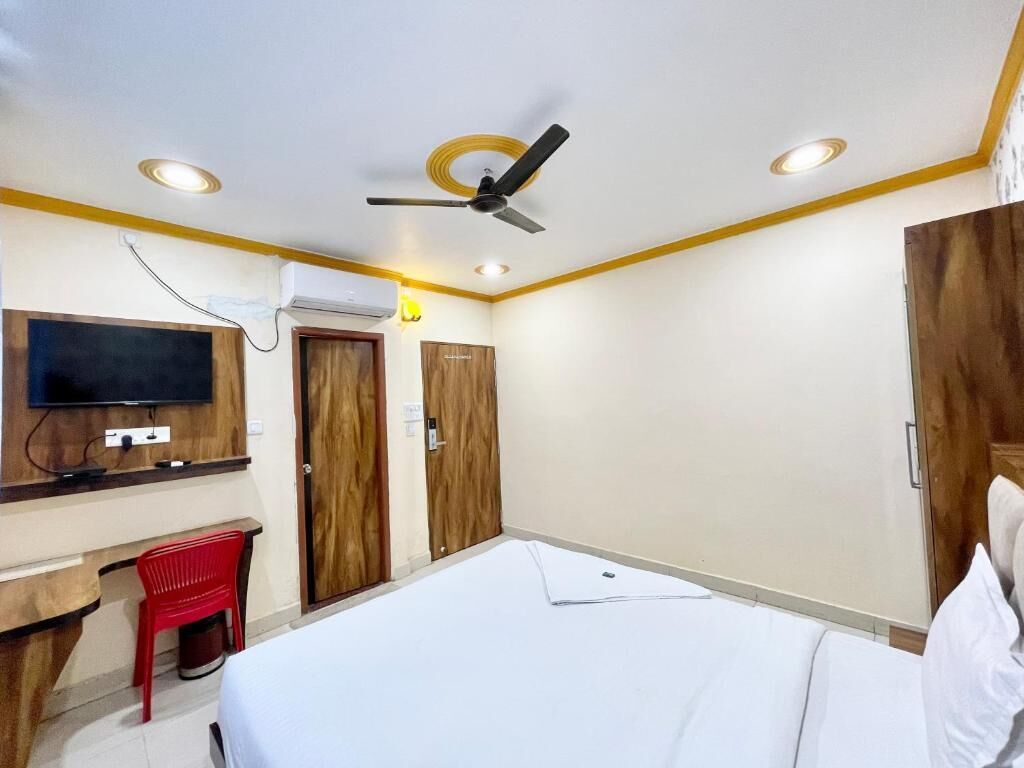 Una habitación de hotel con cama, escritorio, televisión y ventilador de techo.