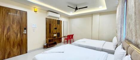 A hotel room with two beds, a ceiling fan, a desk, and a red chair.