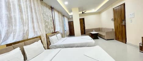 A hotel room with two beds, a sofa, a ceiling fan, and a door with a sign.