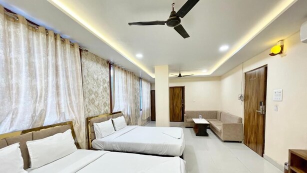 A hotel room with two beds, a ceiling fan, a sofa, and a small table. - Hotel Rudra - near Ghats and Temple (Varanasi)