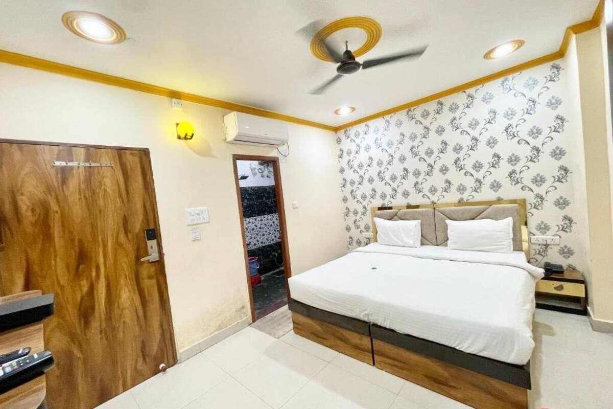 A bedroom with a bed, wooden wardrobe, ceiling fan, and patterned wallpaper.