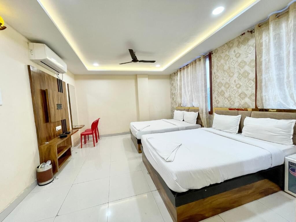 A hotel room with two beds, a ceiling fan, an air conditioning unit, a wooden wardrobe, a red chair, and a small table.
