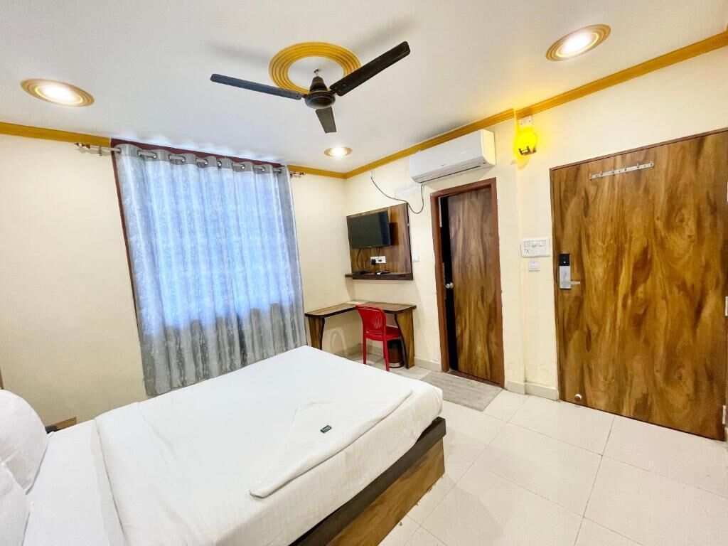 A hotel room with a bed, a desk, a chair, a ceiling fan, and a television.