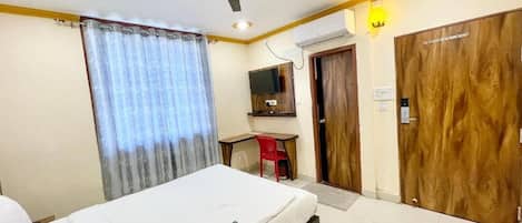 A hotel room with a bed, a desk, a chair, a ceiling fan, and a television.