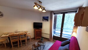Ein Wohnzimmer mit rotem Sofa, einem Holzesstisch, Stühlen, einem kleinen Couchtisch und einem Fernseher auf einer Holzkommode.