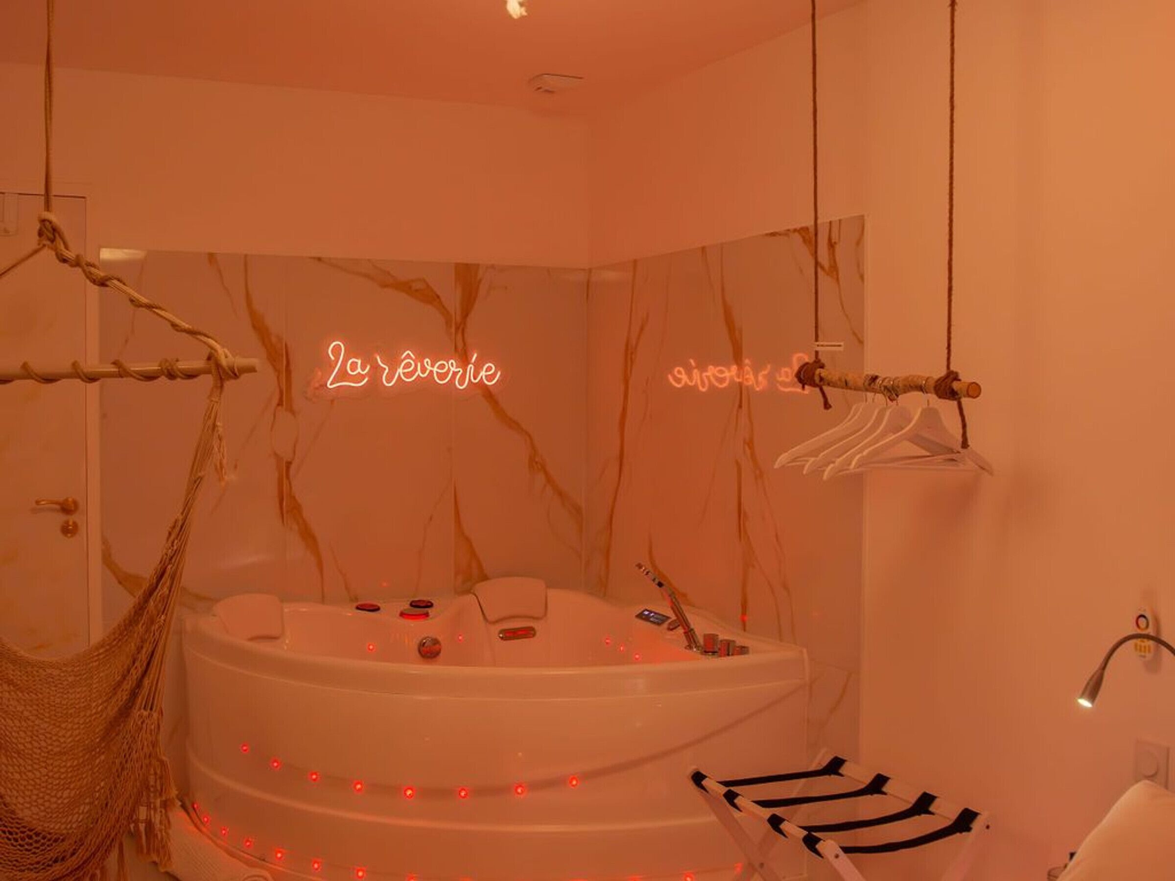 Une salle de spa dotée d’une grande baignoire, d’un hamac et d’un néon.