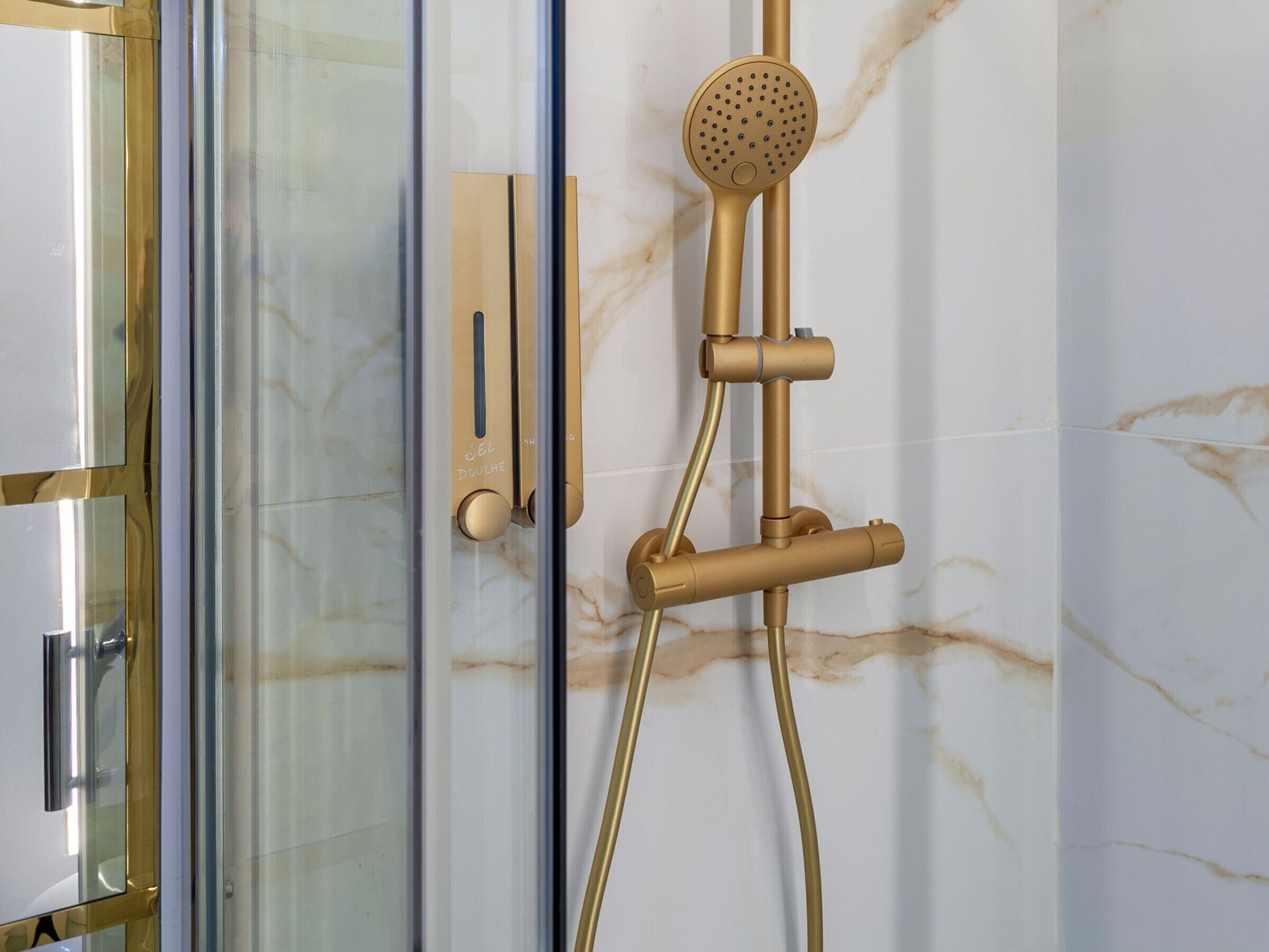 Un bagno moderno con cabina doccia in vetro, soffione dorato e parete in marmo.