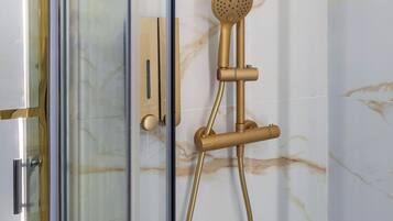 Un bagno moderno con cabina doccia in vetro, soffione dorato e parete in marmo.