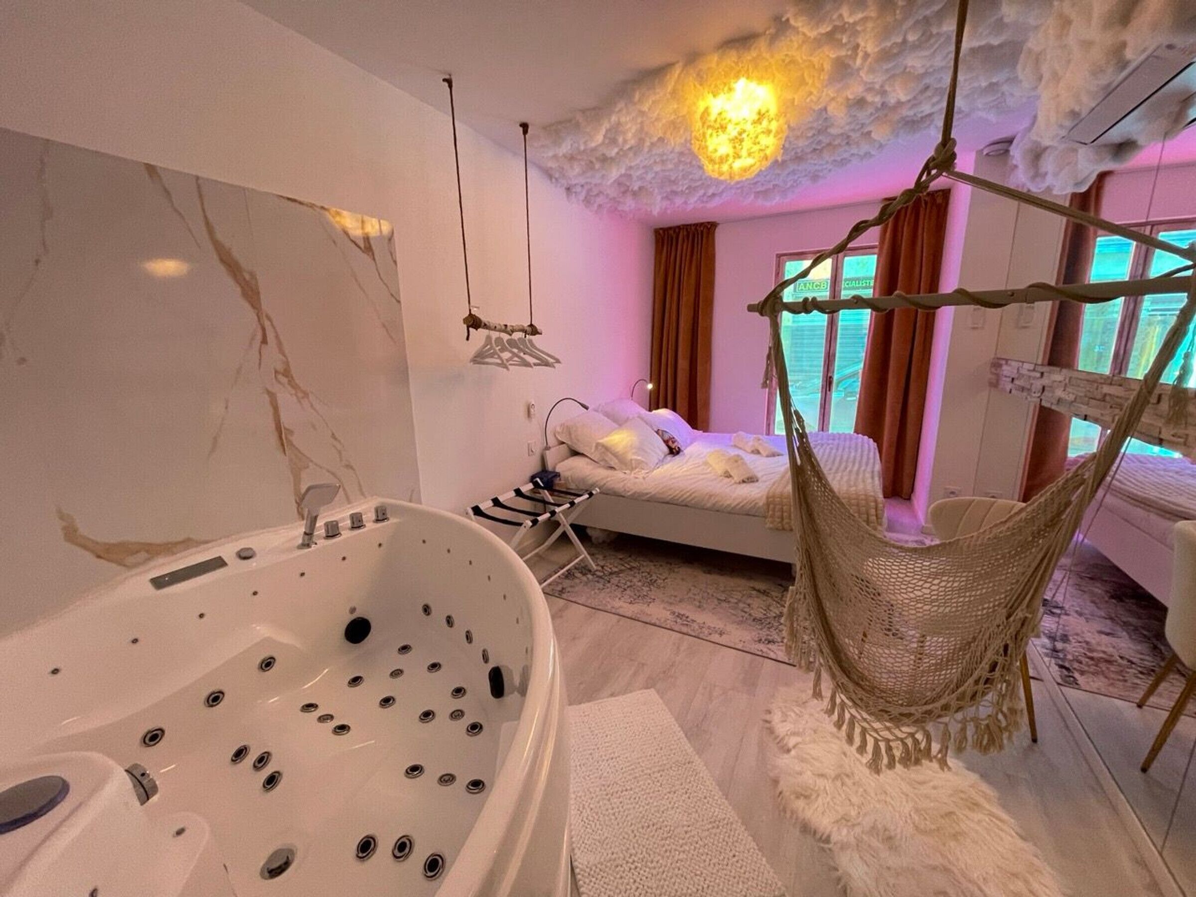 A modern bedroom with a large bathtub, a hanging chair, and a bed with a canopy.