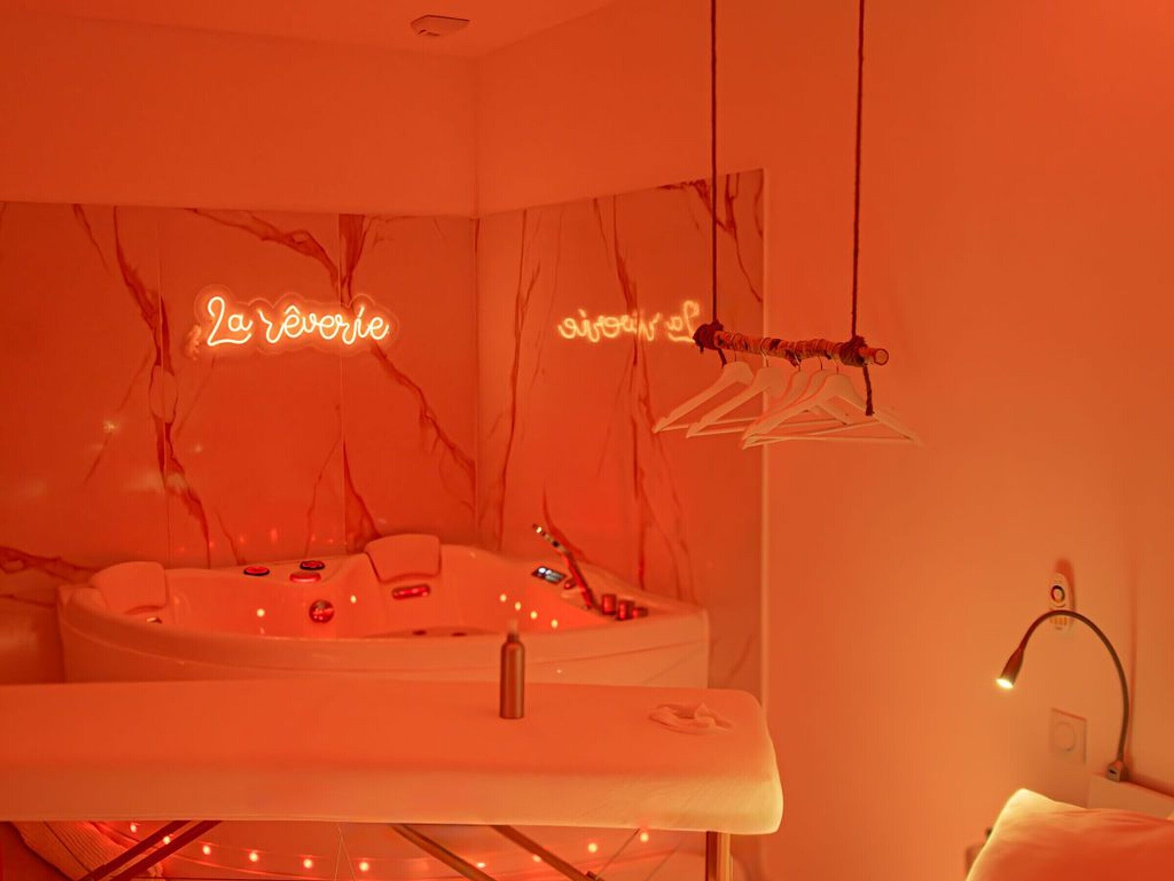 A room with a marble wall, a bathtub, a mirror, and a neon sign.