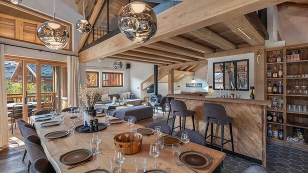 A spacious dining area with a long wooden table set for a meal, a bar area with shelves of bottles, and a cozy seating area with sofas and a fireplace.