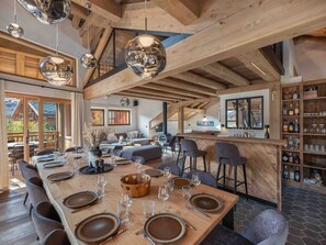 A spacious dining area with a long wooden table set for a meal, a bar area with shelves of bottles, and a cozy seating area with sofas and a fireplace. - Chalet Méribel Village - 14 people, jacuzzi, sauna, parking (Méribel)