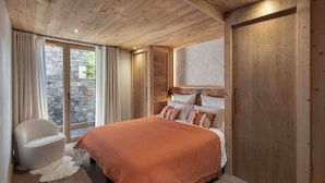 A bedroom with a wooden ceiling, stone wall, and a large bed with a red blanket.