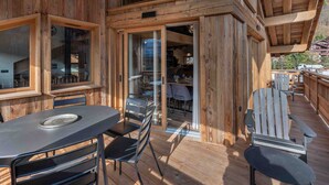A wooden deck with a table and chairs, a glass door leading to an interior dining area, and a view of the surrounding landscape.