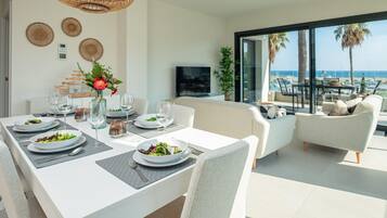 Comedor con una mesa dispuesta para cuatro, televisor y vista a la playa.