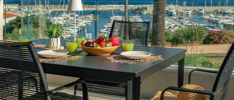 A dining table with a bowl of fruit and drinks, overlooking a marina with boats.