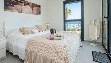 Un dormitorio con cama, una bandeja con tazas y una tetera, vista al mar y una ventana con vista a barcos.