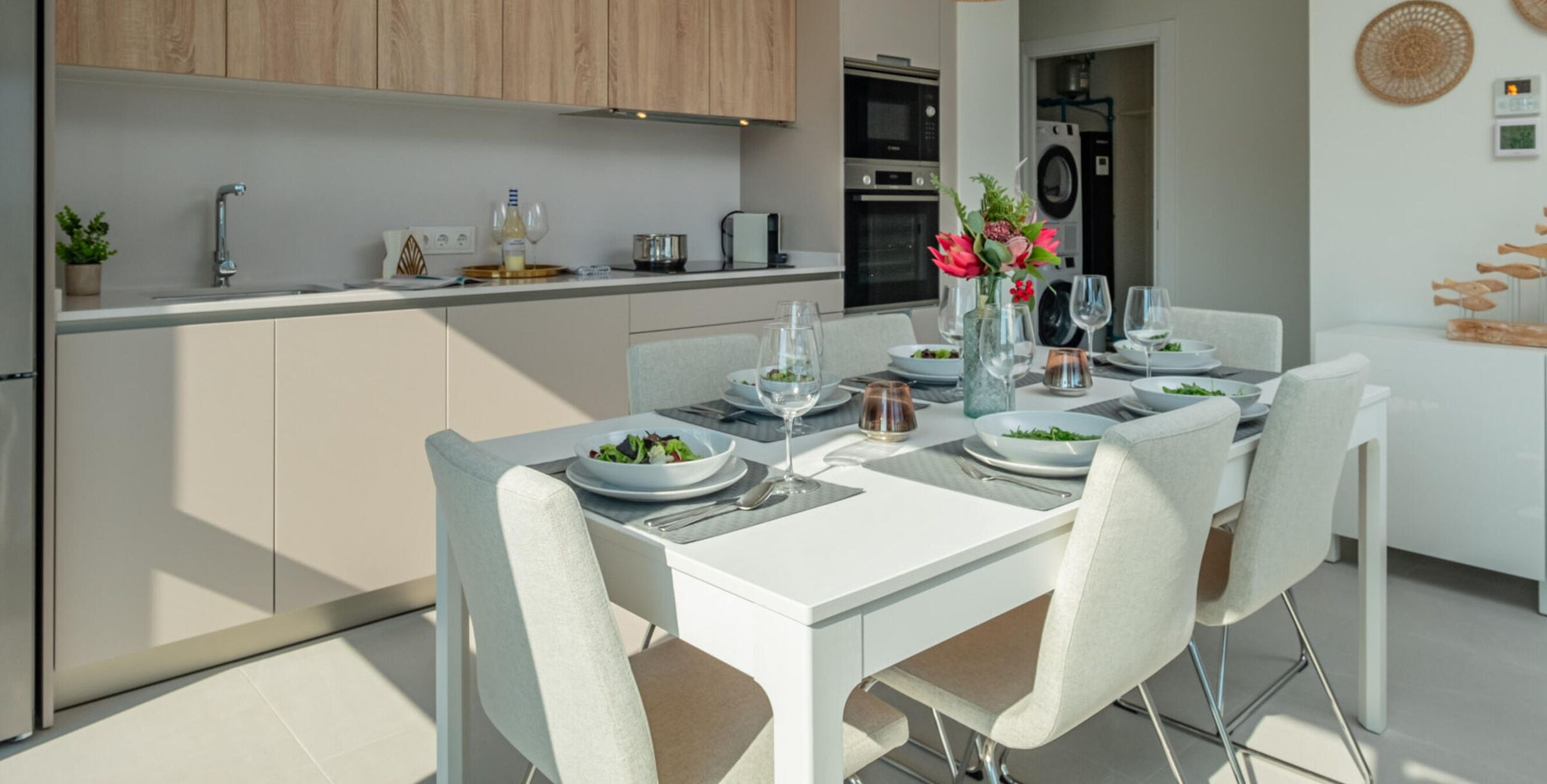 Una cocina moderna con armarios blancos, una mesa de comedor para cuatro personas y un florero con flores sobre la mesa.