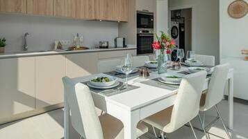 Una cocina moderna con armarios blancos, una mesa de comedor para cuatro personas y un florero con flores sobre la mesa.