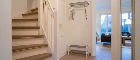 A staircase with carpeted steps leading to a door, a radiator, and a view of a living room with a sofa and a table.