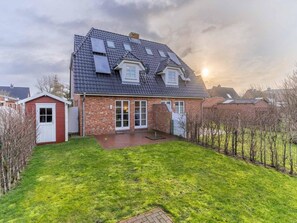 Une maison à deux étages avec une porte rouge, une façade en briques et un toit en pente doté de lucarnes.