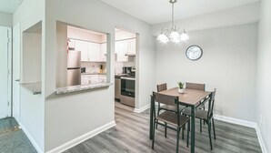 A modern kitchen with white cabinets, a stainless steel refrigerator, and a dining area with a wooden table and chairs. - Barcelo at East Cobb Q5 1 Bd 1Bth Newly furnished (Marietta)